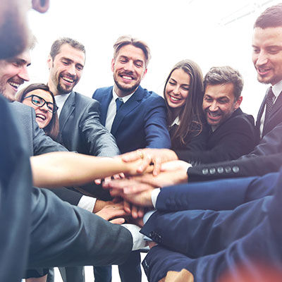 Circle of employees with hands stacked celebrating an event.